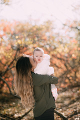 Young mother with little girl in autumn forest with a beautiful colored background