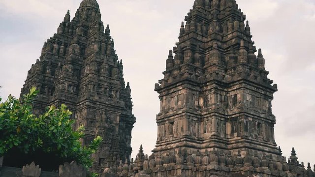 Prambanan temple towers behind stone brick piles and wall in Jogjakarta, Indonesia on cloudy evening, tilt up
