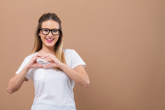 Woman making a heart shaped gesture with her hands on a brown background
