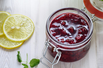 Open jar of raspberry jam next to lemon slices on a wooden white table