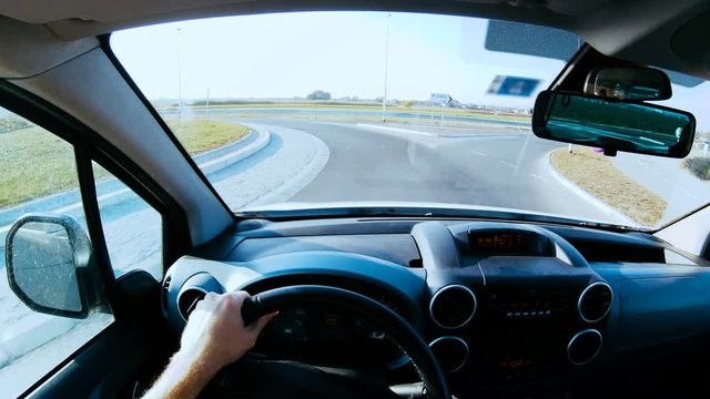 Person POV driving in roundabout slow motion 4K. Driver point of view behind the car wheel in focus while driving on the roundabout and turning to exit.