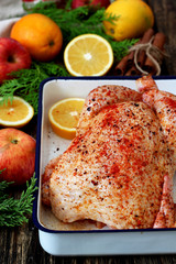 Raw spicy chicken, potatoes and orange slices near apples, cinnamon sticks and cypress branch 