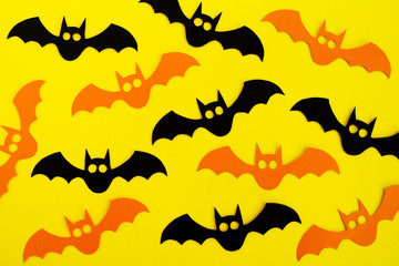 Holiday decorations for Halloween. Black and orange paper bats on a yellow background, top view.