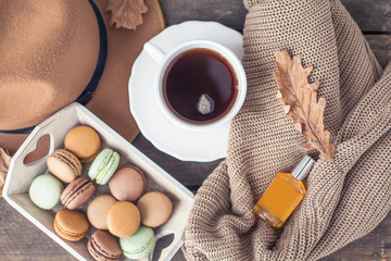 A cup of hot tea, macaroons, a knitted sweater, perfume, a hat, a rug on a wooden table. Autumn. Winter. Cozy.