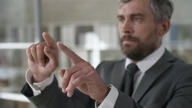 Medium shot of bearded businessman in suit tapping on invisible augmented reality screen, then making spreading multi-touch gesture. Footage suitable for adding AR graphics