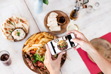 Woman taking photo of mix grill dish using smartphone in restaurant. Bali island. Indonesia.