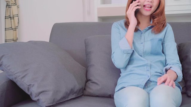 Portrait of beautiful attractive young smiling Asian woman talking on smart phone with friends while lying on the sofa when relax in living room at home. Enjoying time lifestyle women at home concept.