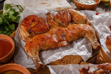 Gentle chicken Tabaka on a wooden background with sauces of different types.