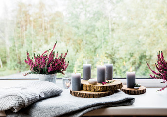 Ready for autumn. Common heather flower in zinc pot, home decor idea.  Set of cozy seasonal decorations on window sill. Gray candles lit, wooden boards, common pink heather flower in flower pot.