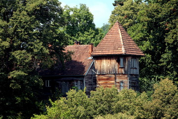 Wooden house shaped like a small castle and in need of restoration completely surrounded with tall trees and other forest vegetation on warm summer day