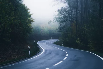 Papier Peint photo Nature Eine Straße schlängelt sich mit vielen Kurven durch den Nebel Wald
