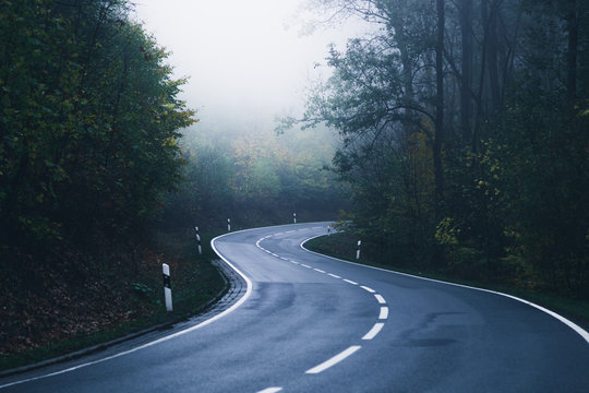 Eine Straße schlängelt sich mit vielen Kurven durch den Nebel Wald