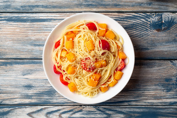 Spaghetti pasta with pumpkin, cherry tomatoes and parmesan cheese in white bowl on vintage wooden background. Top view. Copy space.