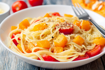 Spaghetti pasta with pumpkin, cherry tomatoes and parmesan cheese in white bowl on vintage wooden background. Selective focus.