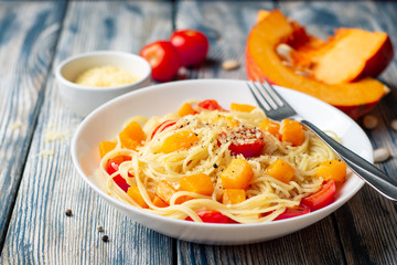Spaghetti pasta with pumpkin, cherry tomatoes and parmesan cheese in white bowl on vintage wooden background. Selective focus.