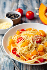 Spaghetti pasta with pumpkin, cherry tomatoes and parmesan cheese in white bowl on vintage wooden background. Selective focus.