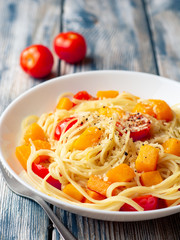 Spaghetti pasta with pumpkin, cherry tomatoes and parmesan cheese in white bowl on vintage wooden background. Selective focus.