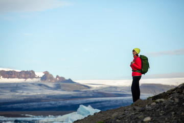 Young sporty girl with backpack admires beautiful view of the ice lake and mountains. Ice lagoon in Iceland