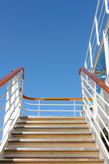 Stairs with railing to climb to the upper deck on a cruise ship against the blue sky.