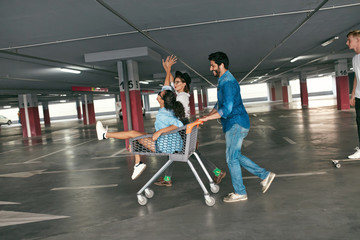 Fototapeta premium Young People Having Fun, Racing On Shopping Trolley At Parking