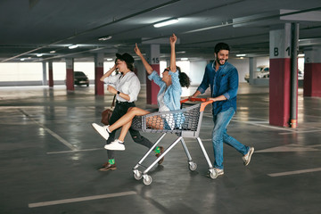 Young People Having Fun, Racing On Shopping Trolley At Parking