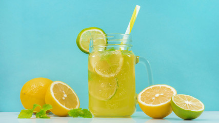 Lemonade drink of soda water, citrus and mint on the light blue background. Cocktail glass with handle and straw, sliced lemon and lime, front view