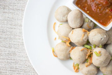 Boiled pork balls with sweet spicy sauce in white plate on gray table mat; top view