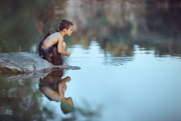 Caveman boy sitting on the rock near river or lake and looking away. Evolution survival concept....