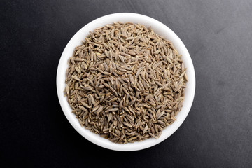 cumin seeds in ceramic bowl top view on black background