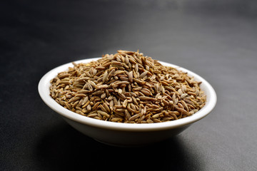 jeera in ceramic bowl , cumin seeds on black background