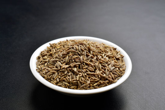 cumin seeds in white bowl on black background