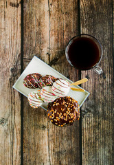 Colorful donuts and black coffee on wooden table. Morning breakfast.
