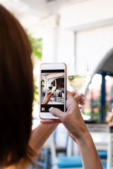 Woman taking photo of white wine on her smartphone in restaurant. Bali island.