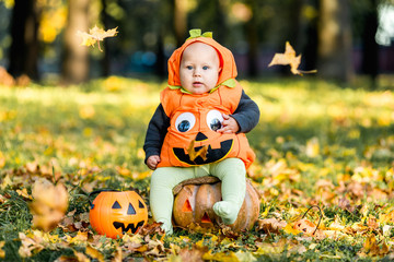 Child in pumpkin suit on background of autumn leaves
