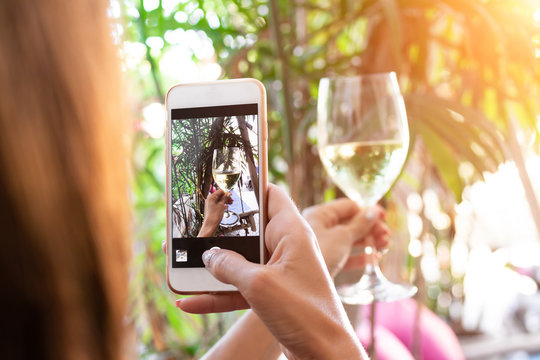Woman taking photo of white wine on her smartphone in restaurant. Bali island.