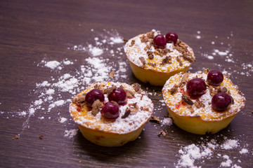 Muffins with cherries and powdered sugar and chocolate chips on a dark wooden background.