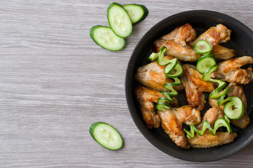 Pan-fried chicken wings and green cucumber on wooden background.
