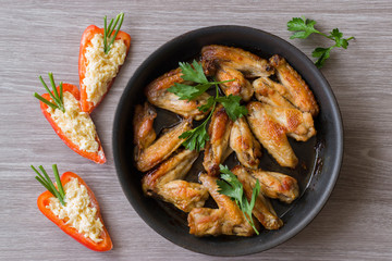 Pan-fried chicken wings and orange paprika with grated cheese on wooden background.