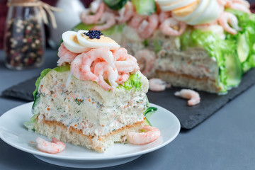 Piece of traditional savory swedish sandwich cake Smorgastorta with bread, shrimps, eggs, caviar, dill, mayonnaise, cucumber and lettuce, horizontal