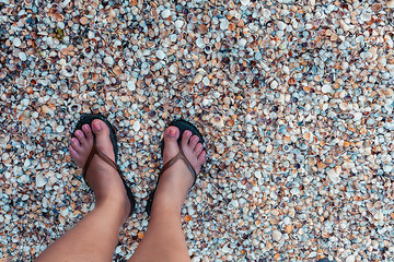 POV of a woman's feet in flip-flops on the beach