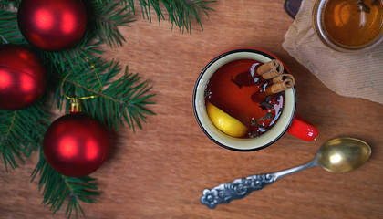 Obraz na płótnie Canvas Hot Christmas Drink cup of hot aromatic tea with cinnamon sticks and lemon with fir tree branches and red balls on wooden table background. Christmas Happy New Year winter holiday concept. Flat lay