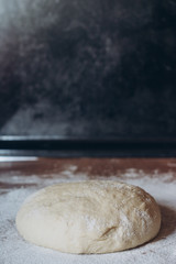 Ball of raw dough sprinkled with flour on rustic wooden counter