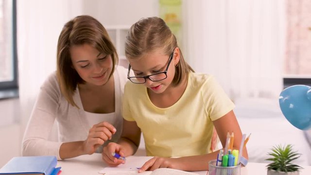 education, family and homework concept - happy mother and daughter with book writing to notebook at home