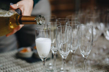 Sommelier pours champagne from a bottle into a glass at the table in the restaurant.