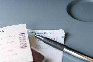 Airplane tray table on seat back inside cabin; passport, ticket and immigration bureau card with sun shining through the window. Travel lifestyle vacations concept. (selective focus)