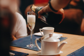 Sommelier pours champagne from a bottle into a glass at the table in the restaurant.