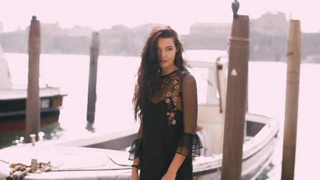 Travel tourist woman standing on the pier against beautiful view on venetian chanal with boats in Venice, Italy. Attractive young romantic girl on vacation walking happy by Grand Canal. Gorgeous mixed