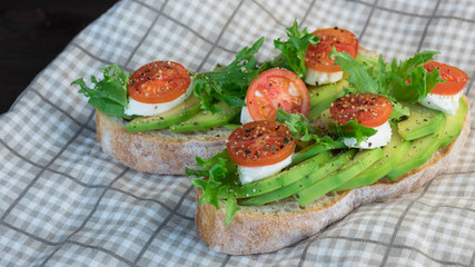 Avocado toasts, cherry tomatoes on a wooden background. Breakfast with toast and avocado, vegetarian cuisine, the concept of a healthy diet. 