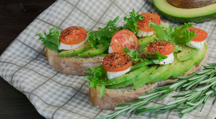Avocado toasts, cherry tomatoes on a wooden background. Breakfast with toast and avocado, vegetarian cuisine, the concept of a healthy diet. 