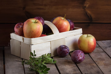 Gifts of autumn: apples and plums in a basket on a wooden background, autumn composition, harvest
